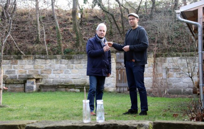 Frank Brandhoff übergibt die Flaschen an Paul Pfund an der Fundstelle im Hinterhof an der Rudolf-Leonhard-Straße